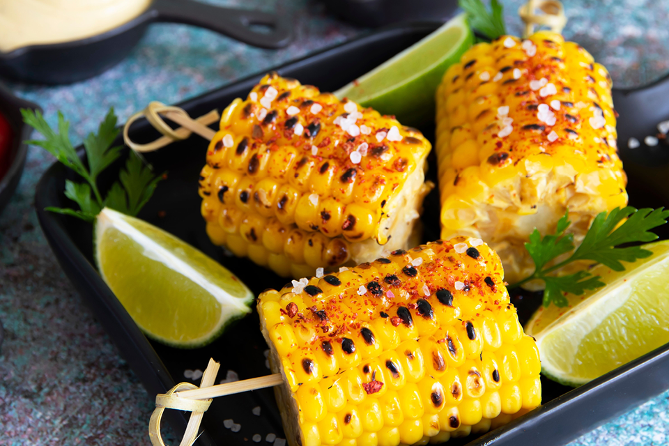 Grilled corn on the cob sprinkled with paprika and garnished with lime slices. 