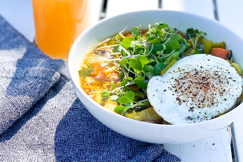 Bowl of soup with vegetables topped with an egg sunny side up