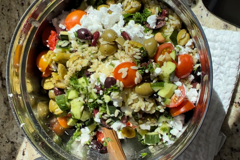 Photo of Greek Orzo Salad featuring green olives, cucumber, cherry tomatoes and more.