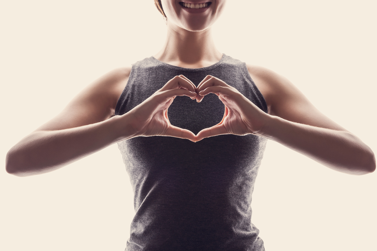 Fit woman holding hands up in a heart shape in front of her chest