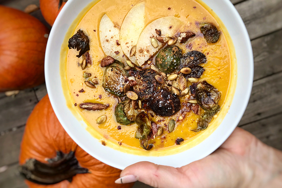 A hand holding a bowl of Butternut Squash, Carrot, and Ginger Soup