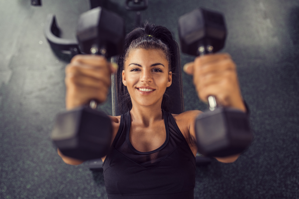 Overhead view of woman doing dumbbell chest press while smiling