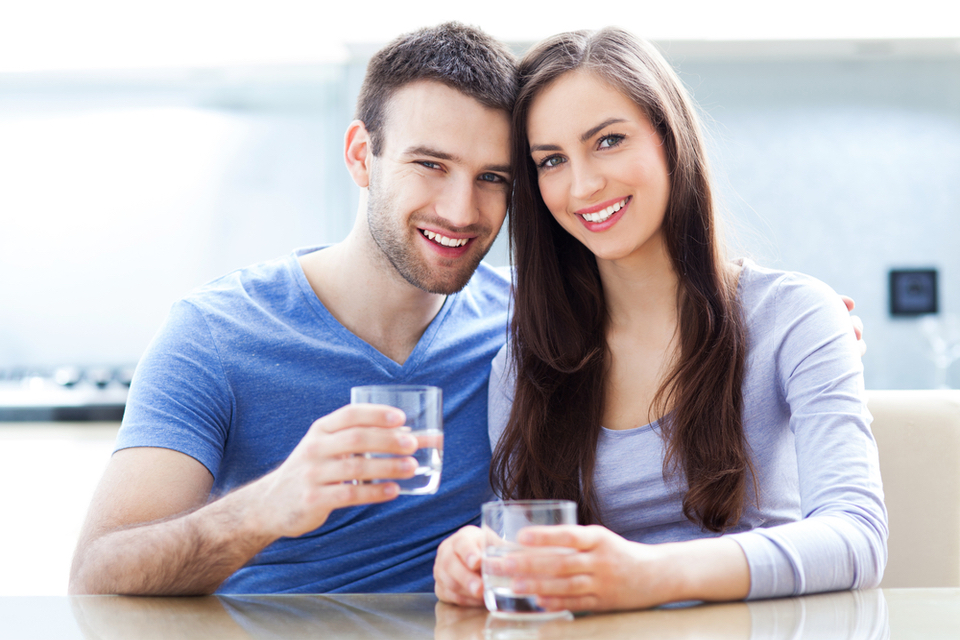 Man and woman holding each other with glasses of water in their hands