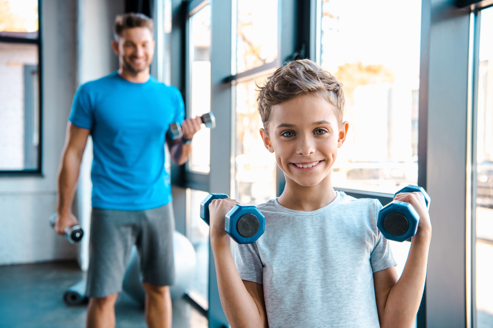 Boy holding dumbbells with his dad behind him