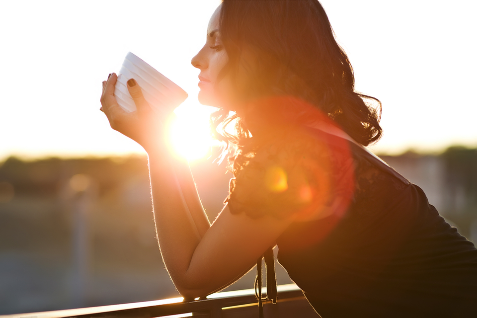 Woman holding mug in front of a sunrise