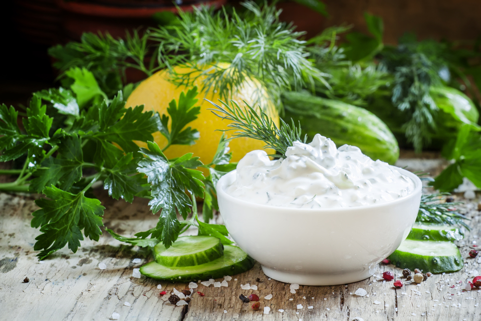 Bowl of greek yogurt with vegetables and greens in the background