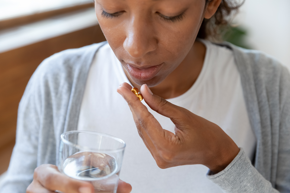 Black woman taking vitamins with water. 