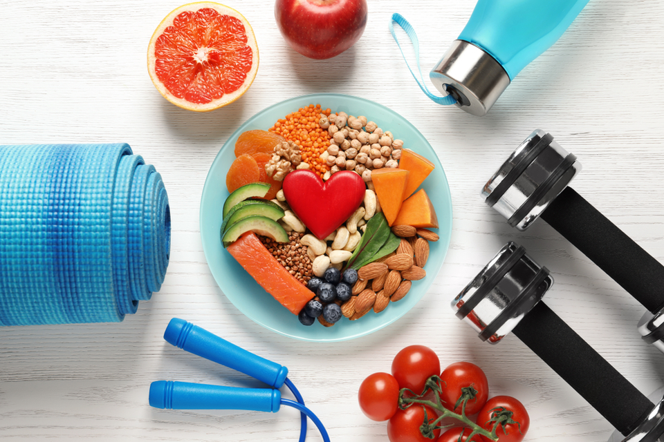 Exercise equipment surrounding a plate full of fruits, vegetables and nuts with a heart in the middle