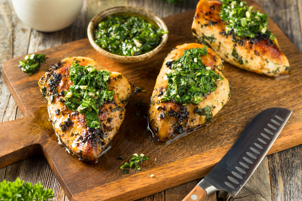 Cutting board with grilled chicken topped with Chimichurri 