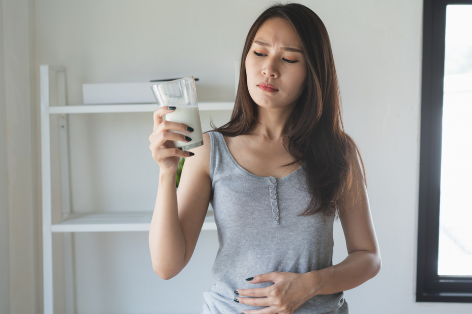 Irritated Woman holding stomach with glass of milk in other hand