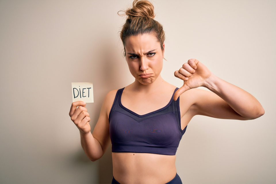 Upset woman with one hand holding a note saying "diet" and the other with a thumbs down