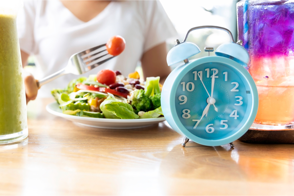 Person eating salad with a clock in front of them