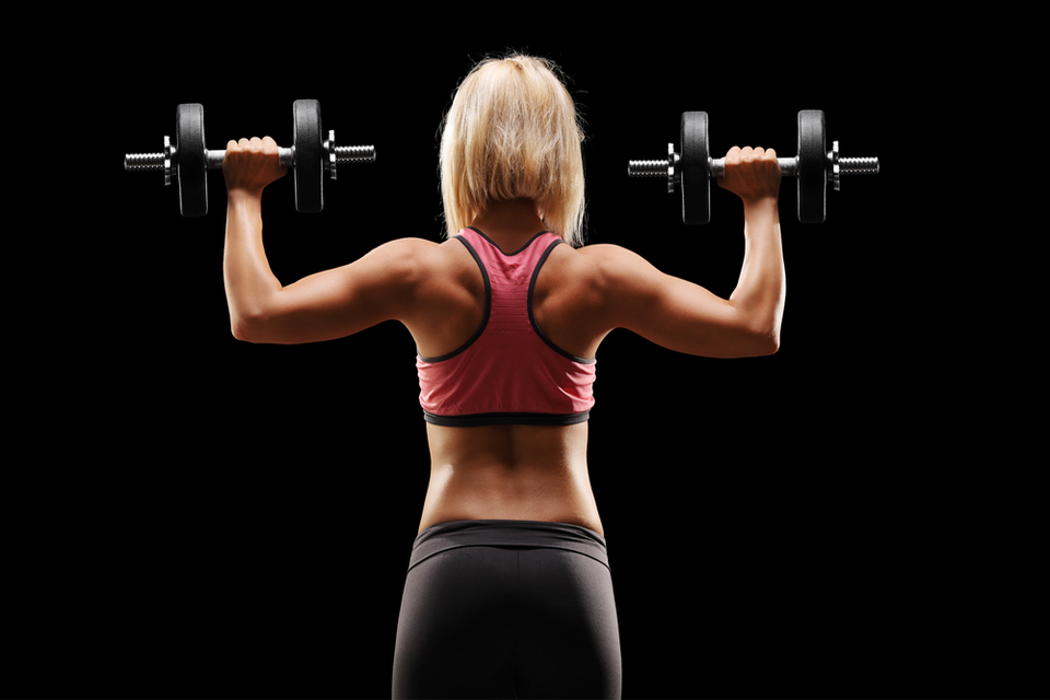 A womans back as she hold up a dumbbell in each hand