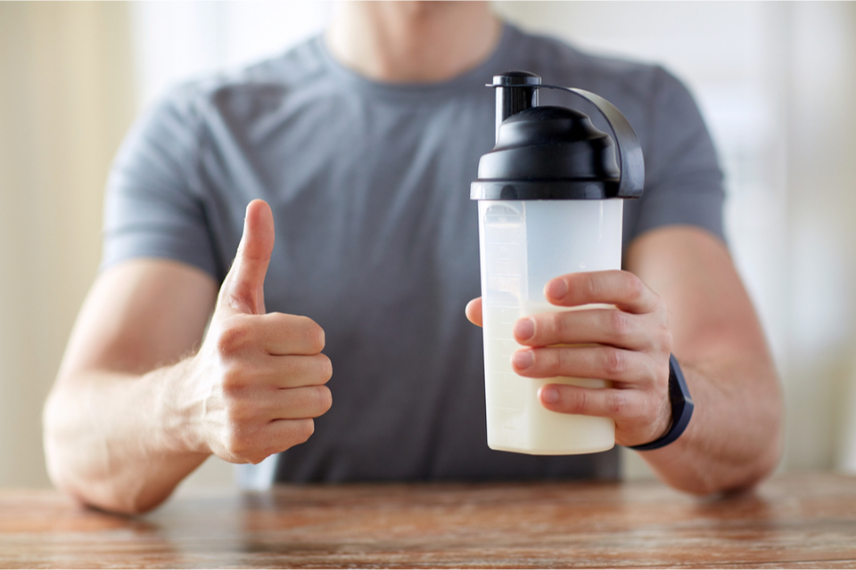 Person holding a protein shake in one hand and holding a thumbs up in the other
