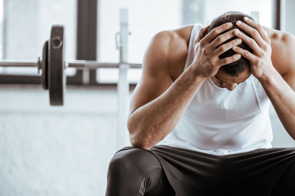 Men hunched over in front of a bench press